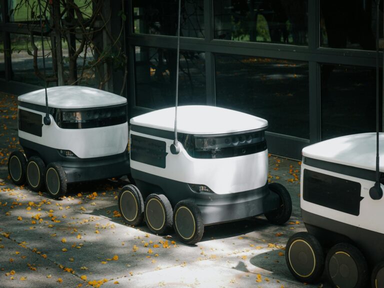 Autonomous delivery robots on a sidewalk during daytime, showcasing modern technology.